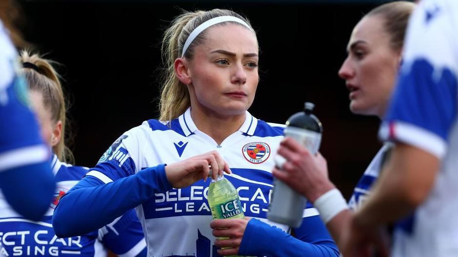 Charlie Estcourt opening a bottle of water during a break in play during a match, wearing a home blue and white Reading FC shirt 