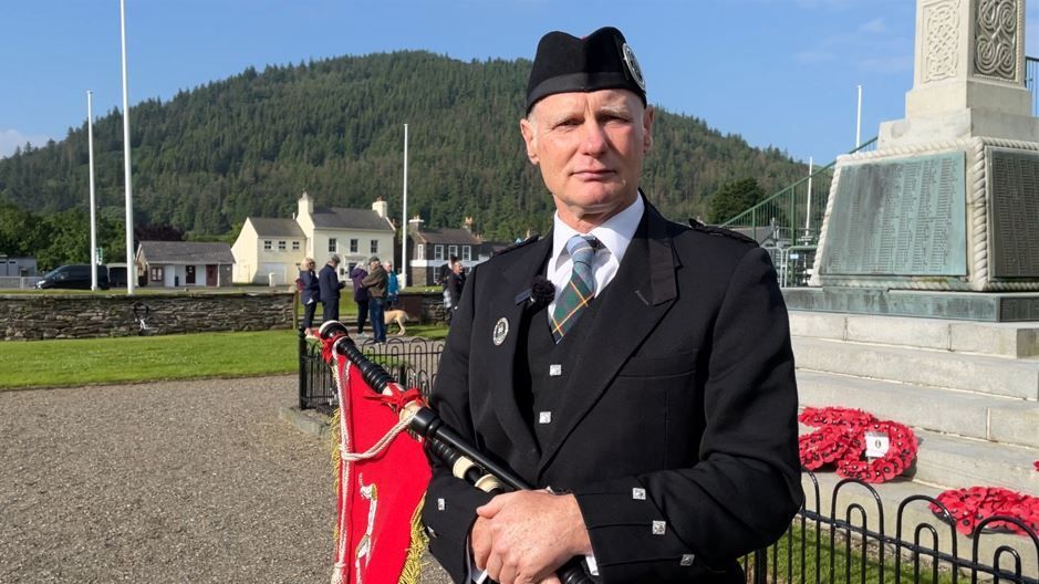 A man holding bagpipes standing in front of a war memorial