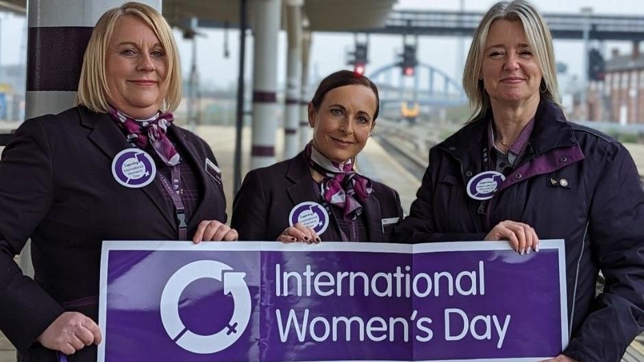 Sara Hardstaff, Sally Ashforth and Maria Alton holding an international womens day banner at Derby Railway Station