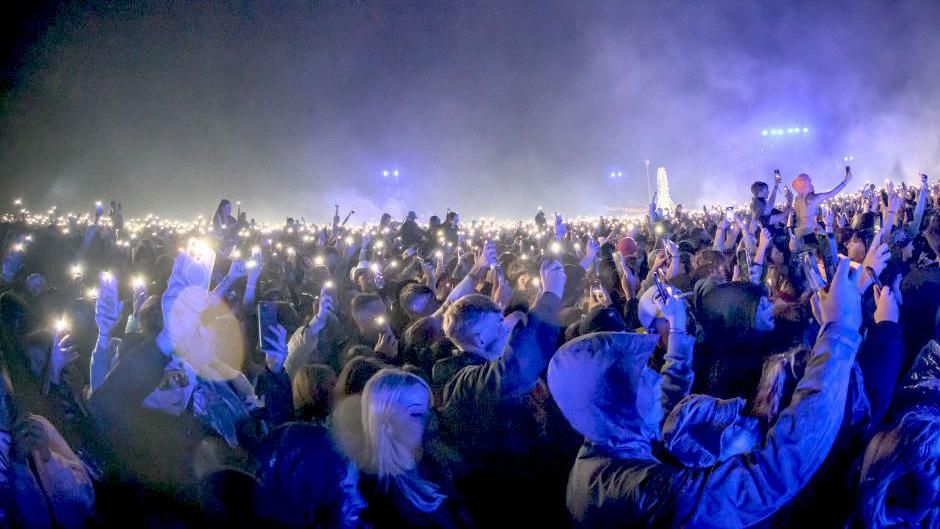 The crowd at Leeds Festival 2024 during a night-time set by Fred Again, lit by blue light from the stage lights and by hundreds of mobile phone torchlights