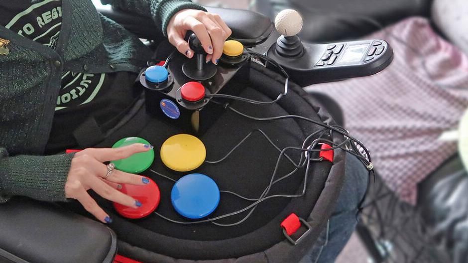 A person playing a game by using a special controller, made up of big coloured buttons and a joystick