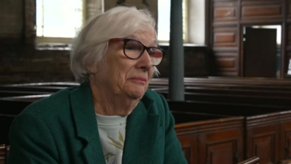 Roberta Higson is wearing a green top and jacket and glasses and is sat in the top tier of the chapel