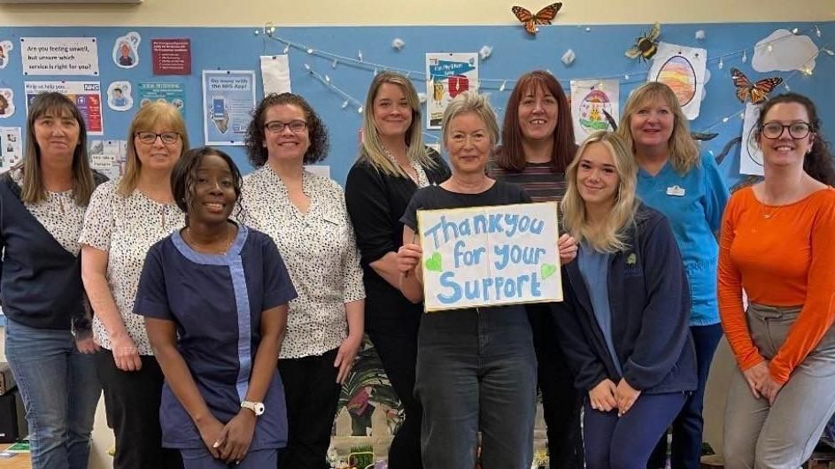 GP with her staff as she holds a "thank you for your support" sign