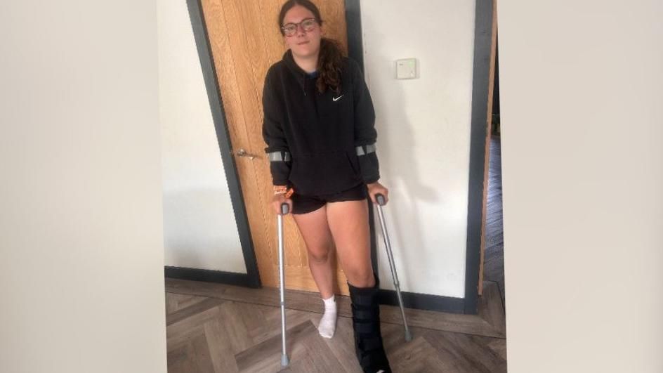 A young woman on crutches with a protective case around her left foot.
