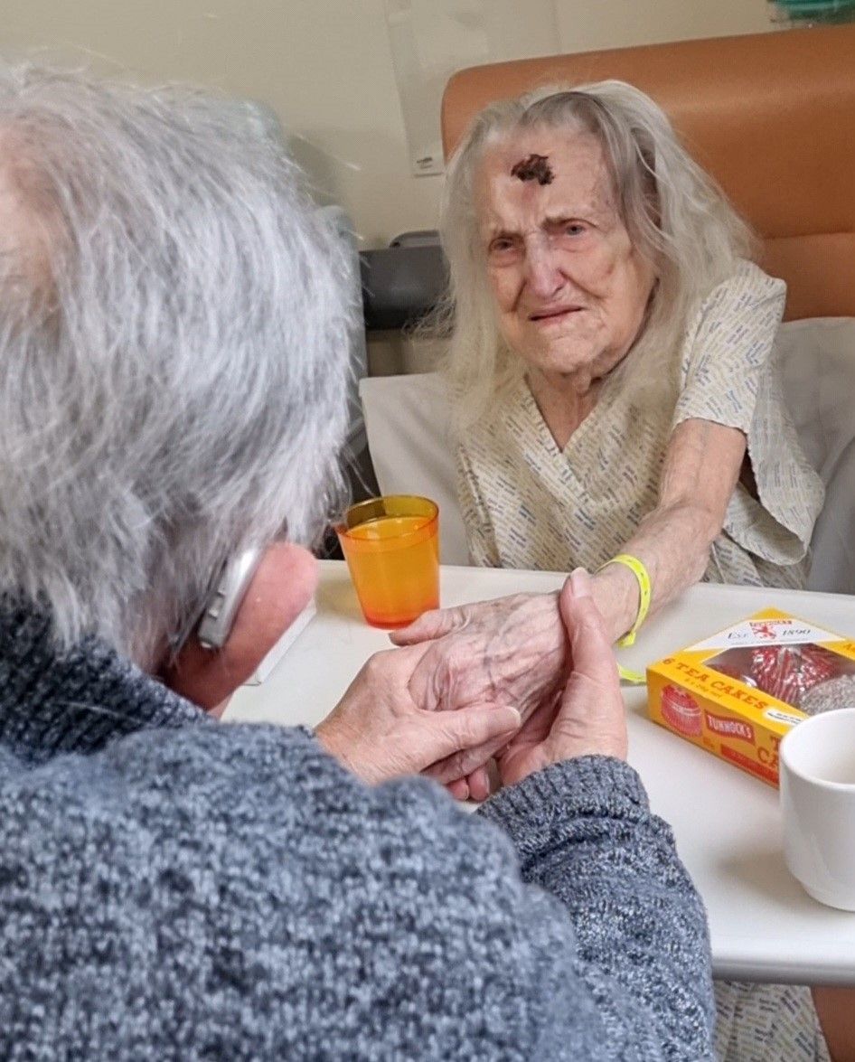 Sheila in hospital bed holding husband's hand