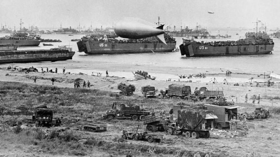 Black and white photo of boats and military vehicles at a muddy beach