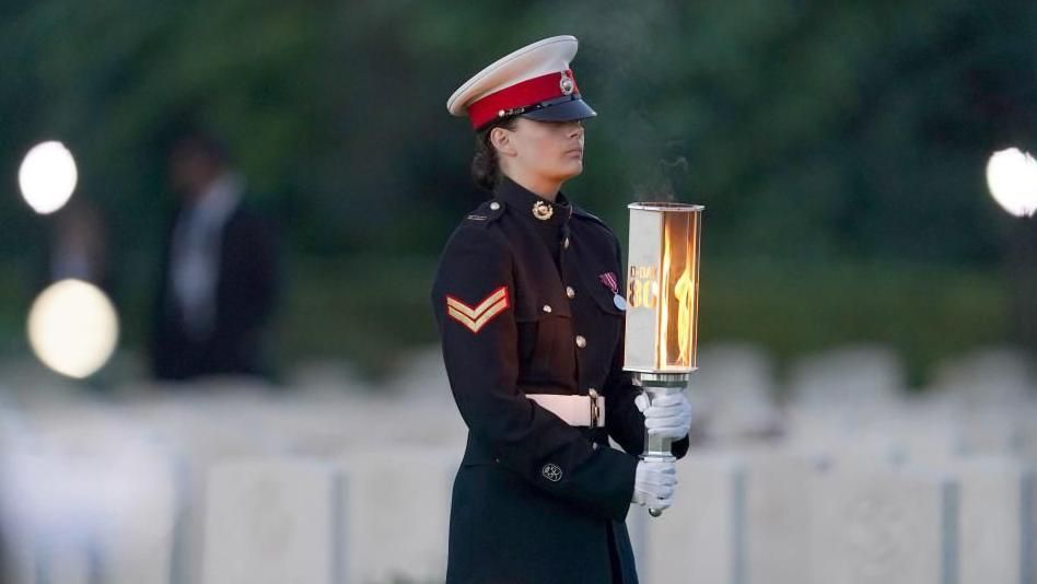 A young woman in military dress carries a torch