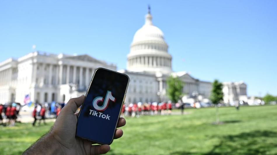 A hand holding a phone with the TikTok logo in front of the US Capitol building