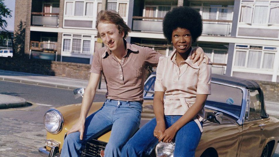 A couple sit on the bonnet of an MG in London, 1970s