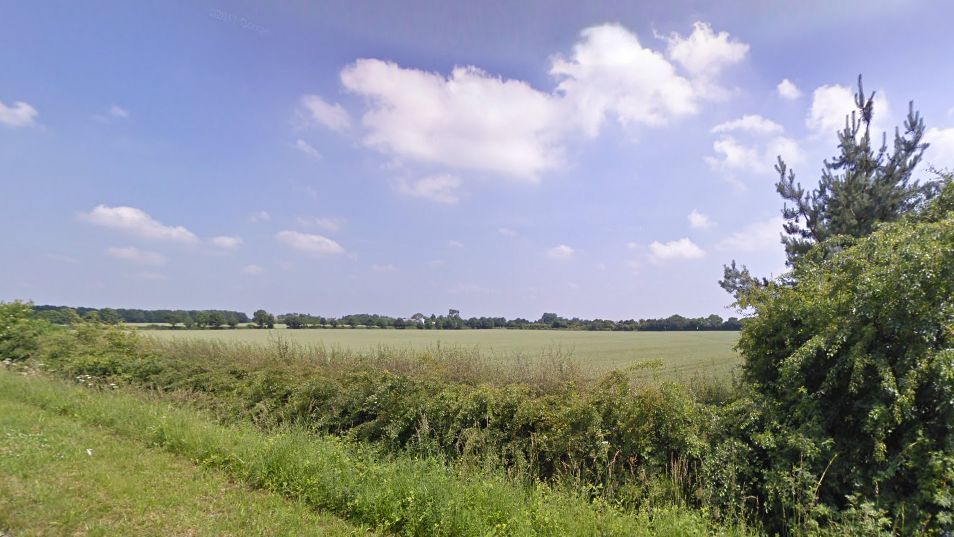 A hedgerow and then green fields, with Hanwell in the distance 