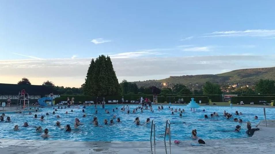 Swimmers in Ilkley Lido on a summer solstice swim, with Ilkley Moor in the background