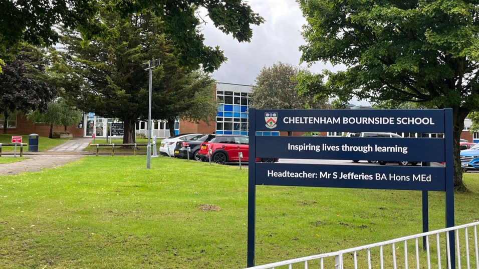 The exterior of Cheltenham Bournside School with a sign out front and several cars parked outside