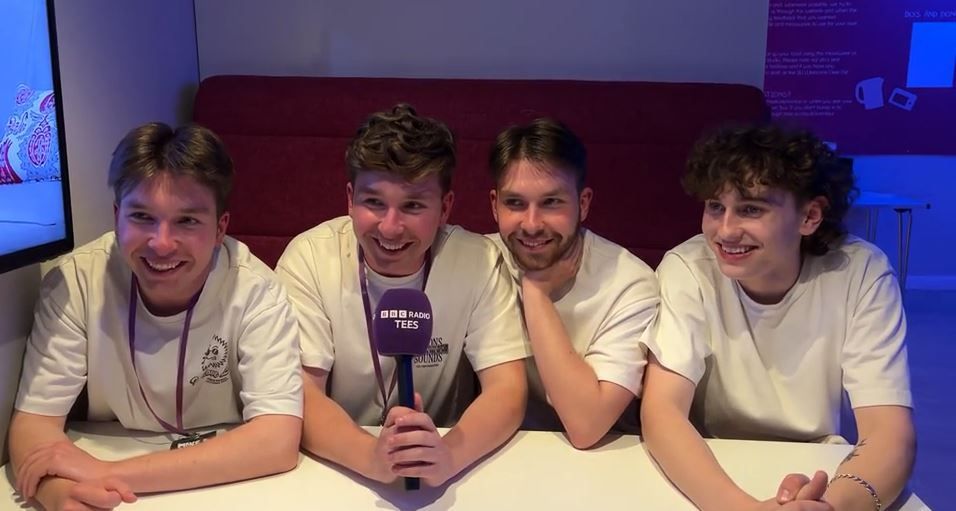 The four members of the band Spilt Milk, seated in front of a microphone