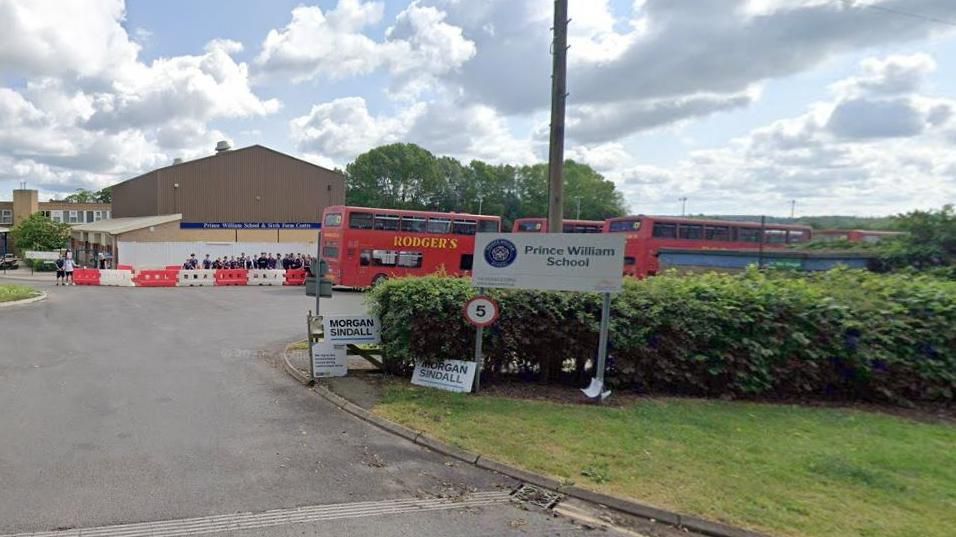 Entrance to school with "Prince William School" sign, showing red buses in the car park