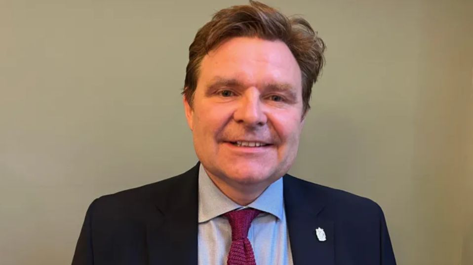 John Cotton, in a dark suit and purple tie looks into the camera