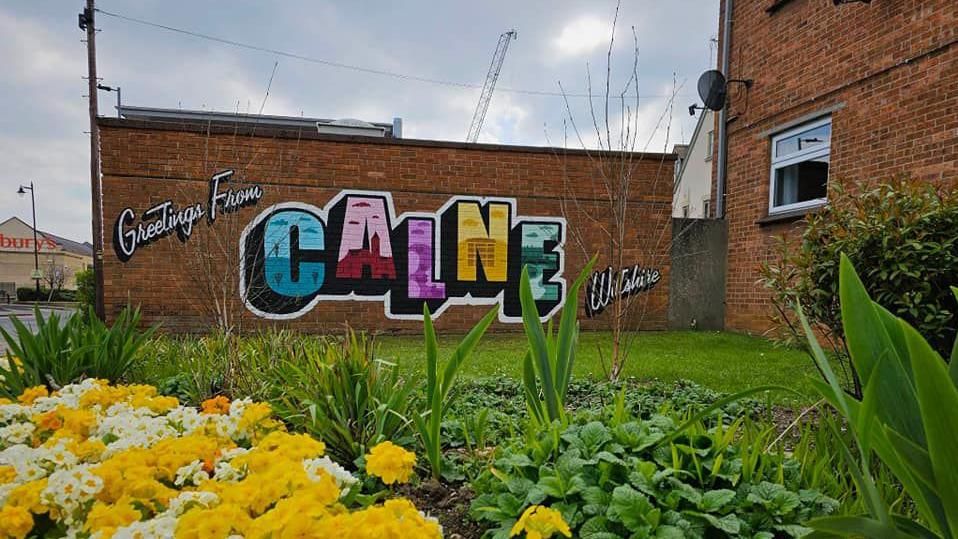 A colourful mural that says 'Greetings from Calne, Wiltshire' on the side of a building