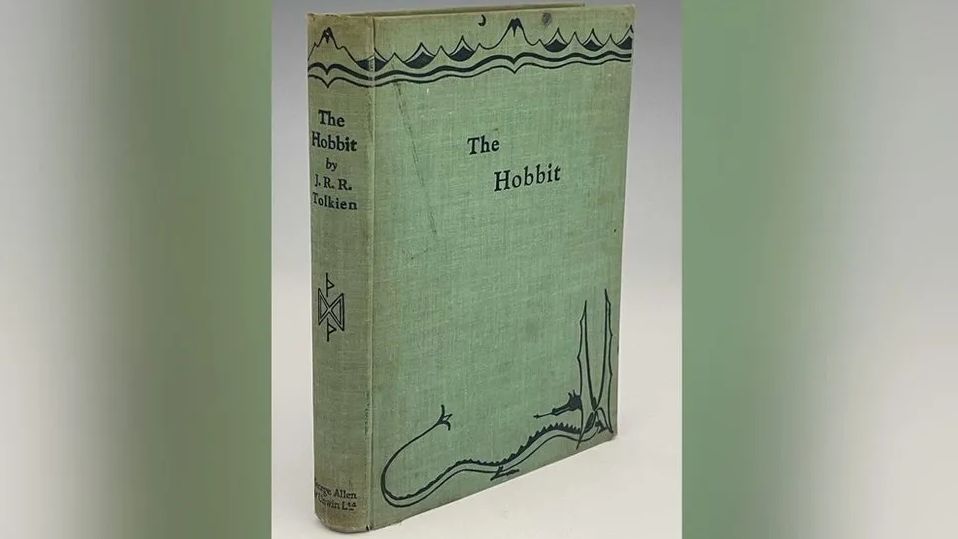 The book without its cover - green and worn with The Hobbit written on the front and spine, snow-capped mountains at the top of the cover and a dragon at the bottom, both in black