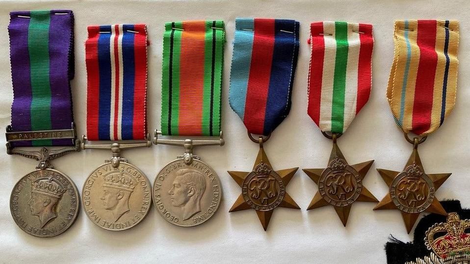 Three circular, silver medals with colourful ribbons, laid on a white cloth alongside three bronze medals shaped like stars with colourful ribbons.