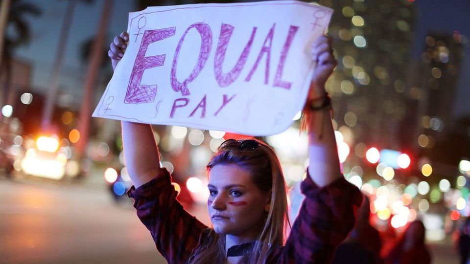 Mujer sostiene un cartel reclamando salario igualitario
