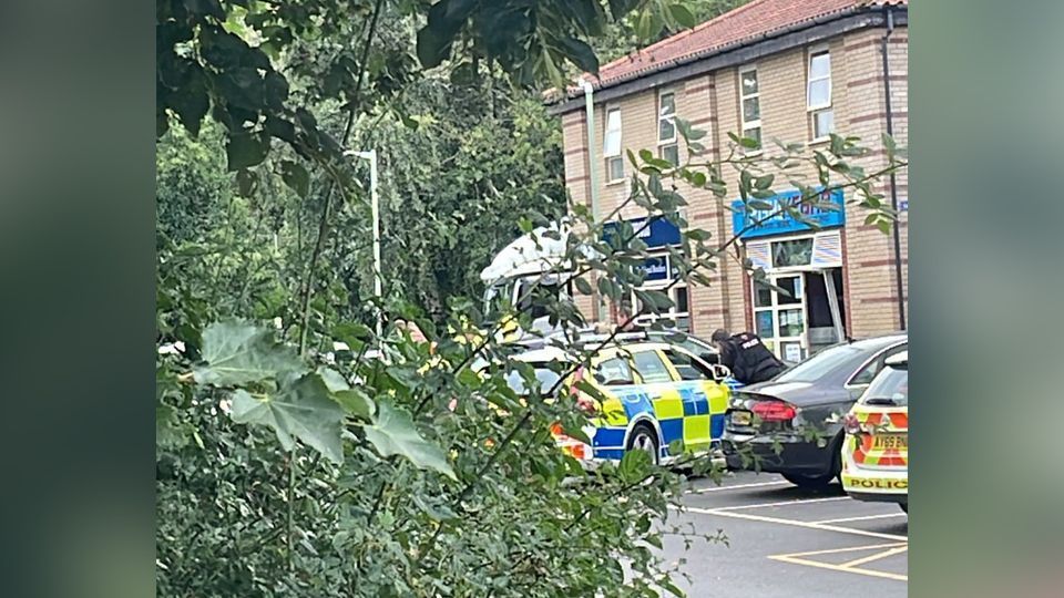 The front of a shop is damaged with police nearby.