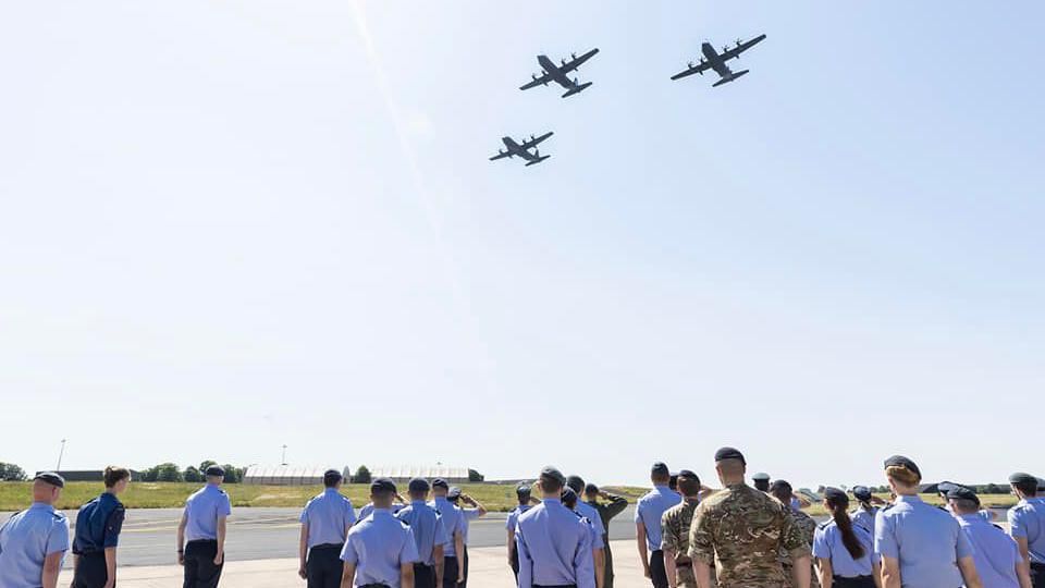 RAF personnel watching three Hercules aircraft fly over Aldergrove Flying Station