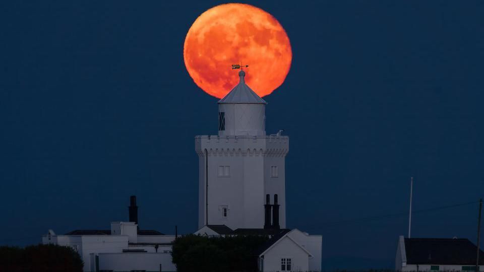 An orange moon behind a lighthouse