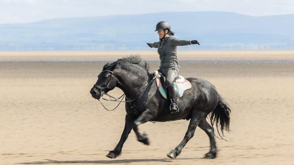 female rider spreads her arms out as she enjoys the ride on her horse