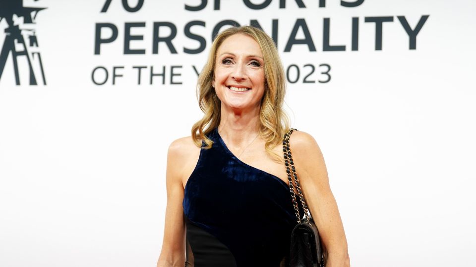 Paula Radcliffe wearing a black dress, smiling, in front of a white background