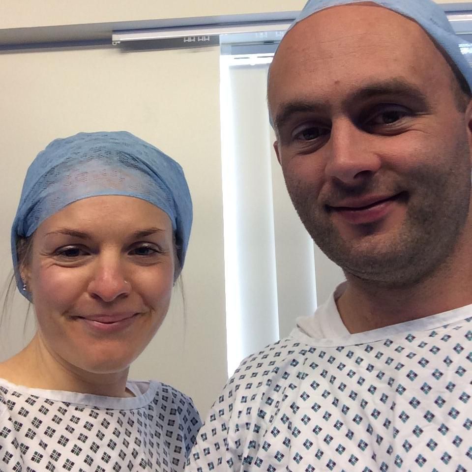 Annika and husband Eulyn smiling at the camera, and wearing medical clothing, during IVF treatment before their son was born in 2018 