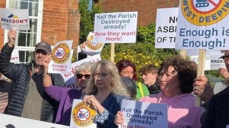 A group of protesters outside a red-brick building in West Deeping. They are holding placards with slogans such as "enough is enough", and "Breedon't".