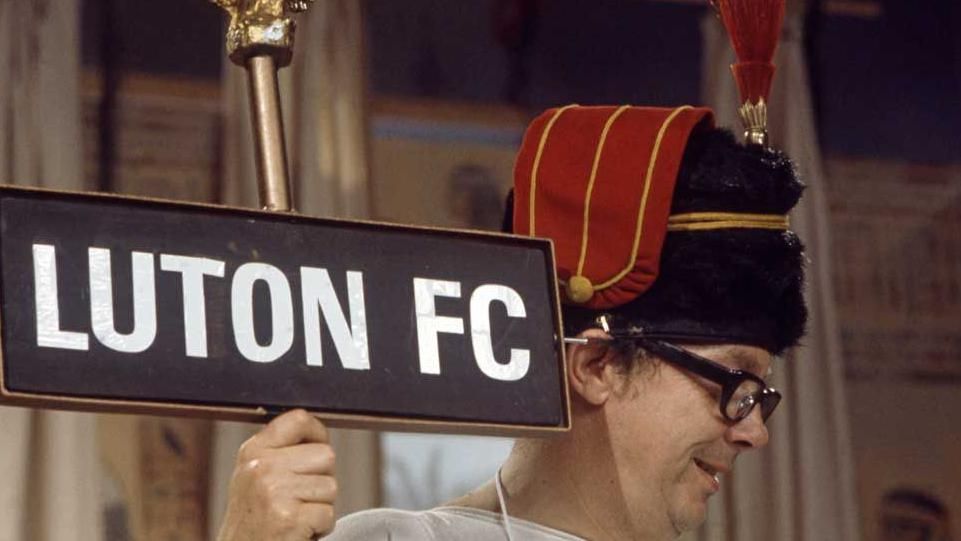 A still from the comedy duo's TV show, showing Eric Morecambe holding a sign that reads "Luton FC"