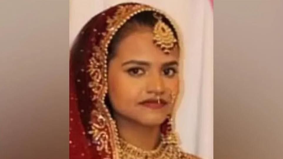 Woman looks at camera while clothed in a sari and wearing lots of gold jewellery on her face and neck