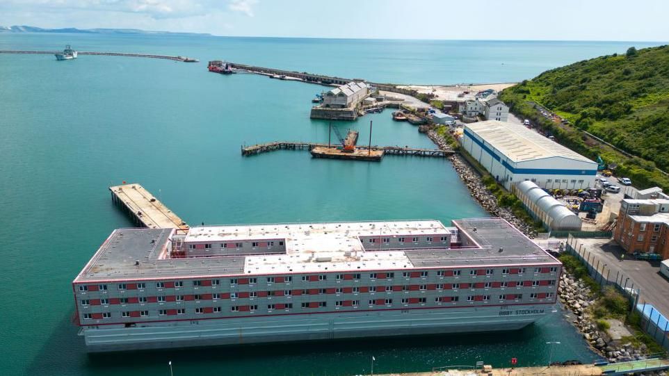 A grey and red barge moored on an island. It is surrounded by the sea.