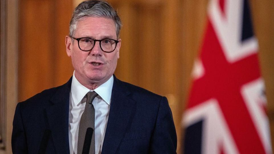 Sir Keir Starmer speaking at a podium with union jack behind him 