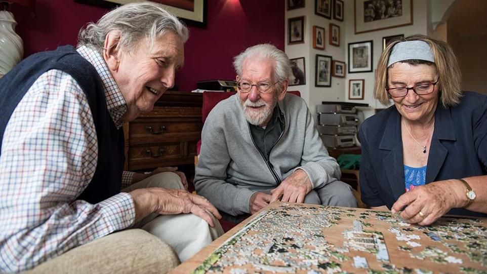 Two elderly men doing a jigsaw with a carer