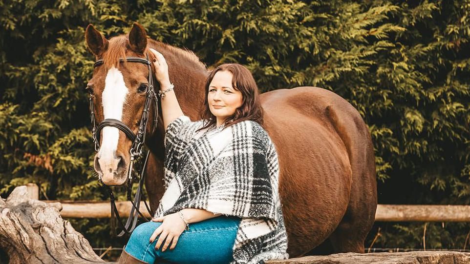 Simone smiling at camera while holding the bridle of a horse