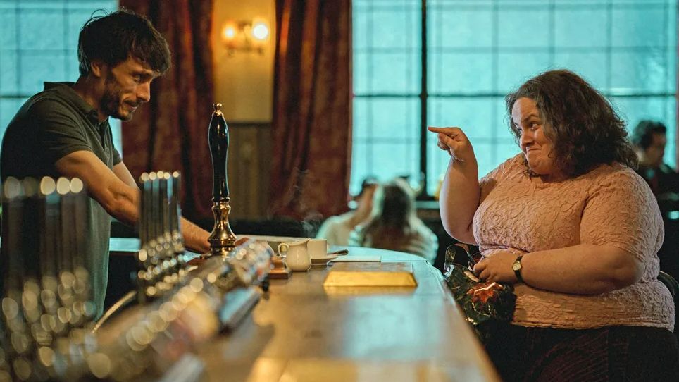 A still image from Baby Reindeer, with Richard Gadd behind the bar, and Jessica Gunning sat in front of the bar 