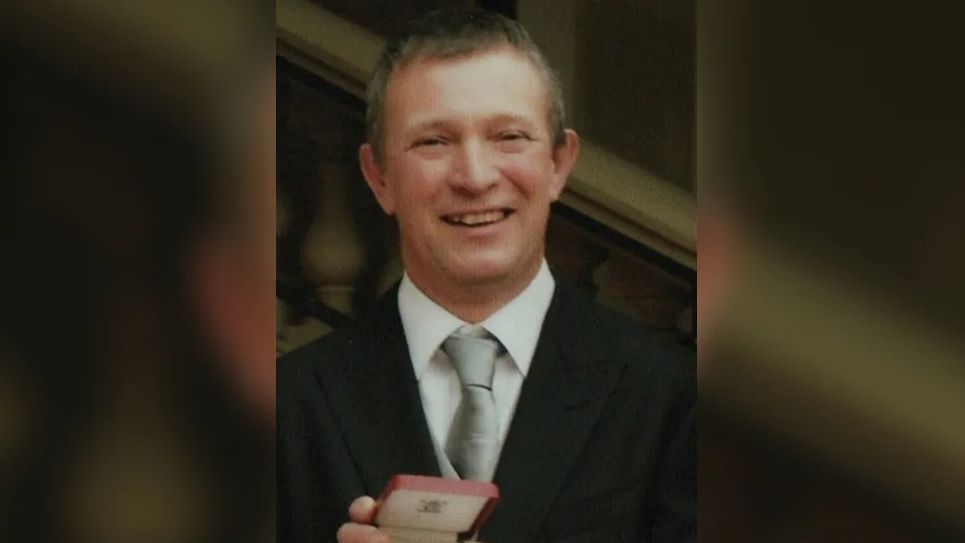 Peter Jeffery smiling at the camera, wearing a black suit, white shirt and silver tie