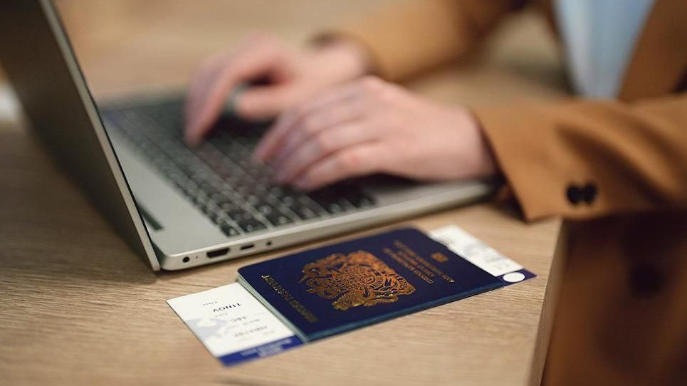 New passport laid out on a table with a person behind it tapping on a computer