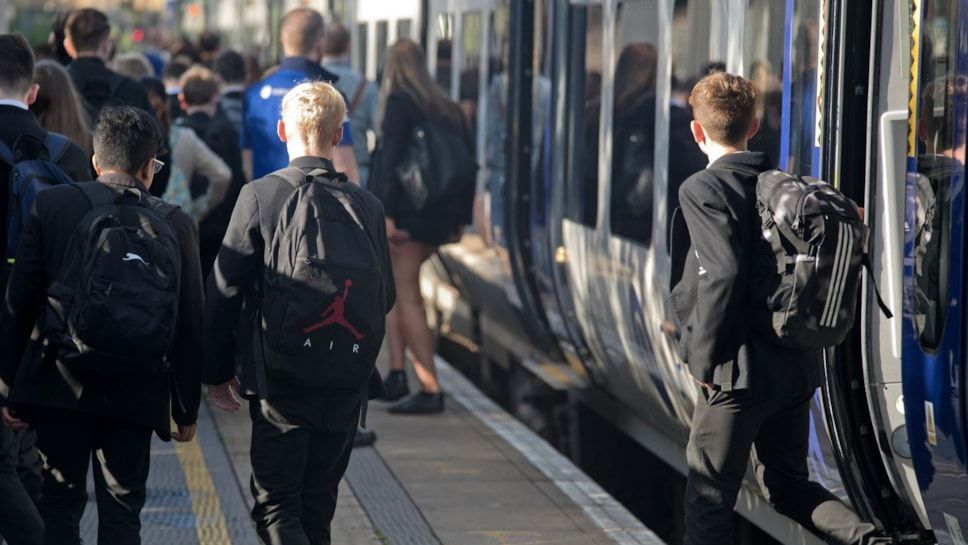 School children at a railway station, having just alighted a train. They are wearing black blazers. 