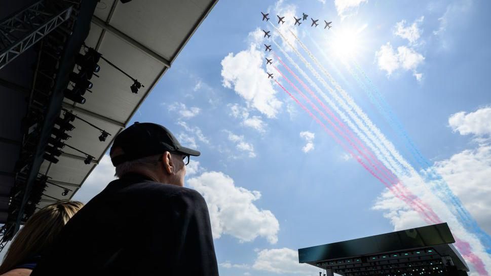 A D-Day veteran in a baseball cap watches the Red Arrows fly over the stadium