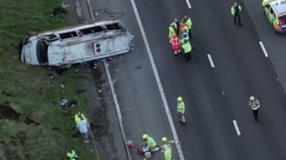 Overturned minibus on the hard shoulder of the motorway with emergency service crews at the scene