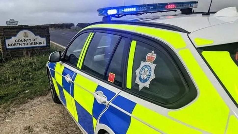 North Yorkshire Police car parked on a road next to the County of North Yorkshire sign