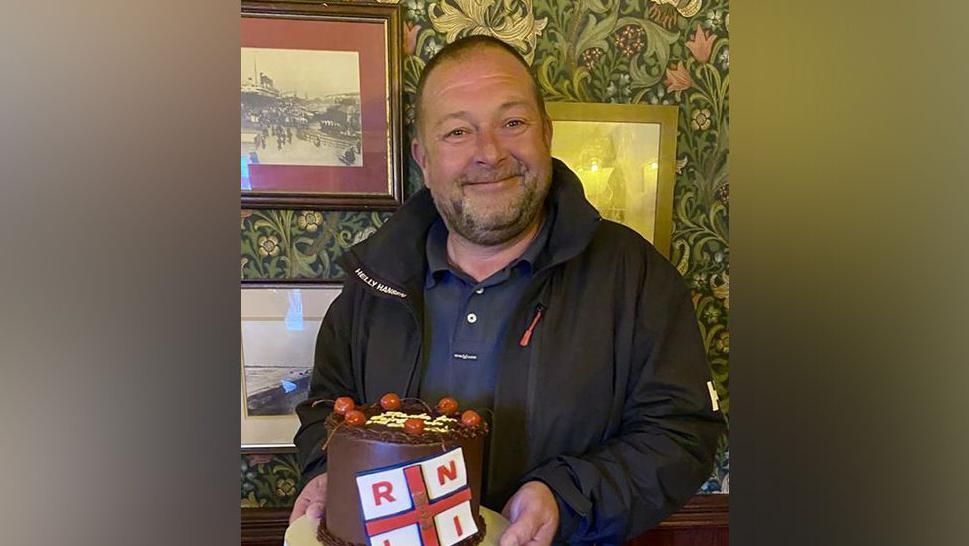 Hoylake RNLI's second coxswain, holding a cake, as he celebrates his retirement