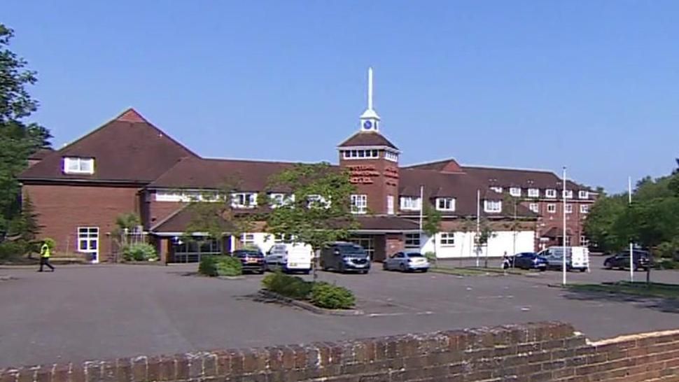 Exterior view of red brick hotel with car park in front. Police van is parked in the car park.