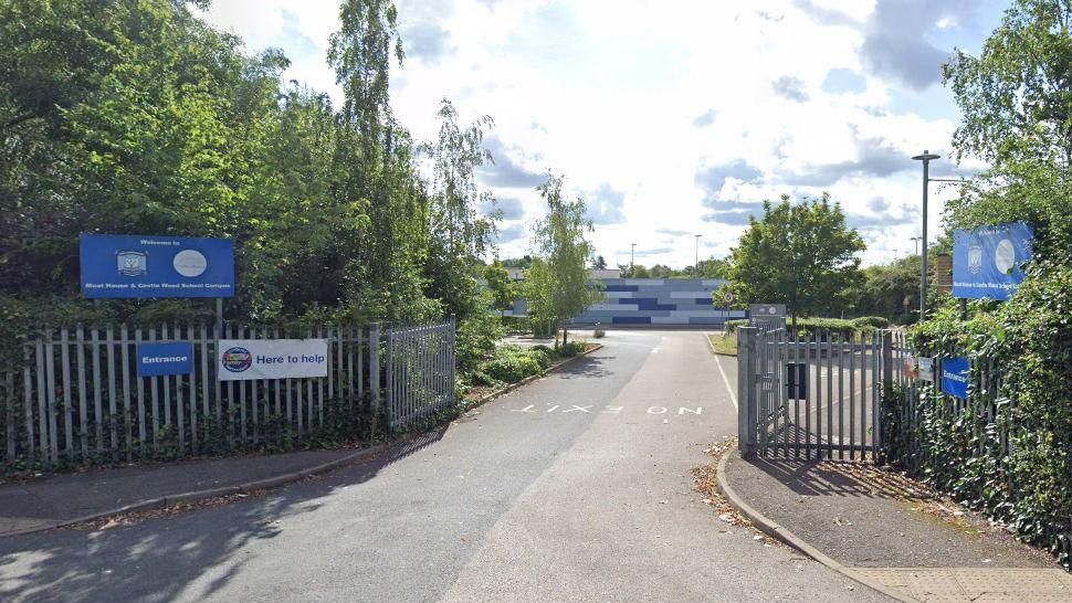 The outside of Castle Wood School with trees and a blue sign with the school's name 