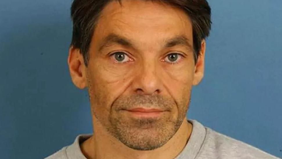 Robert Brown looks directly at the camera for a police mugshot. He has short, dark brown hair and a short shaved beard. He also has blue eyes and is wearing a pale grey sweatshirt