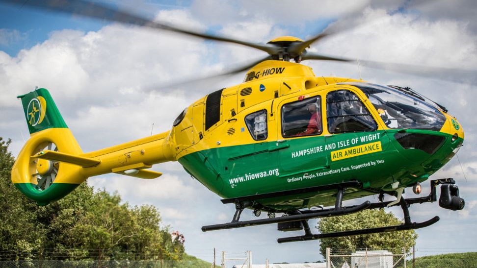 A yellow and green air ambulance helicopter mid-flight