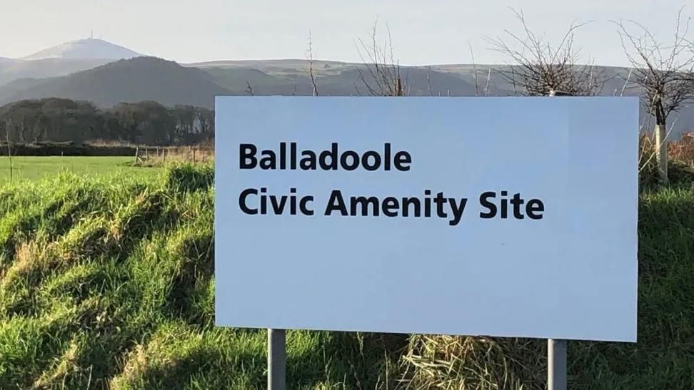 A white sign in front of mountains that reads Balladoole Civic Amenity Site