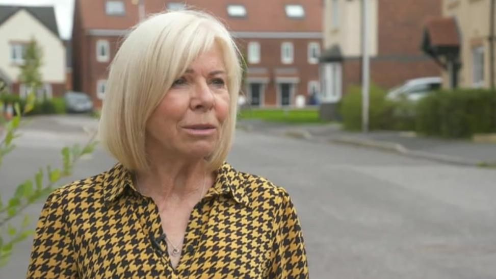 A woman in a black and yellow shirt standing outside in a housing estate